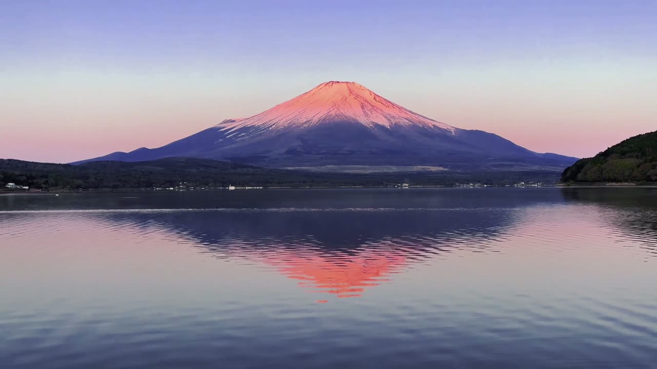 Mount Fuji at dusk, its snow-dusted peak reflected in the still water of a lake