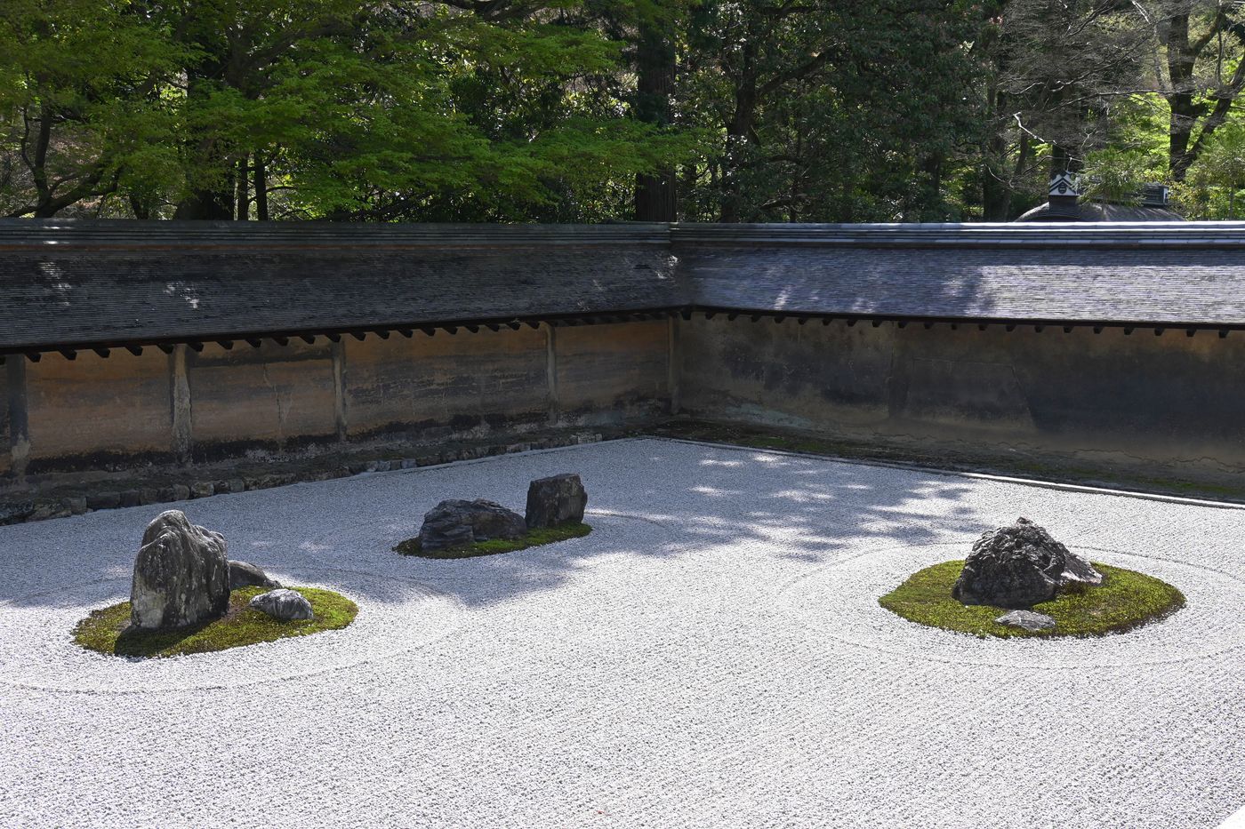 El jardín de rocas karesansui de Ryoan-ji, con sus piedras y su musgo dispuestos sobre grava blanca rastrillada, visto desde una galería de madera.